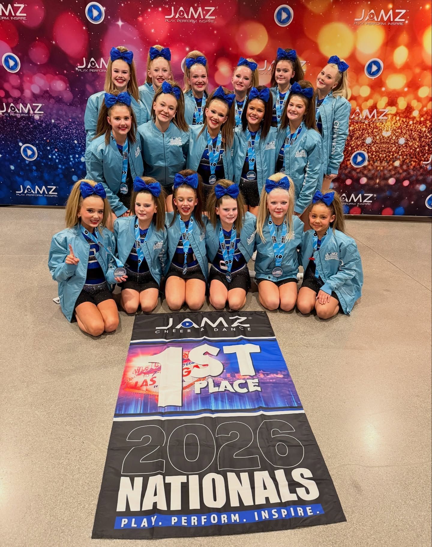 Cheer team in blue uniforms posing with a 1st place 2026 Nationals banner and confetti backdrop