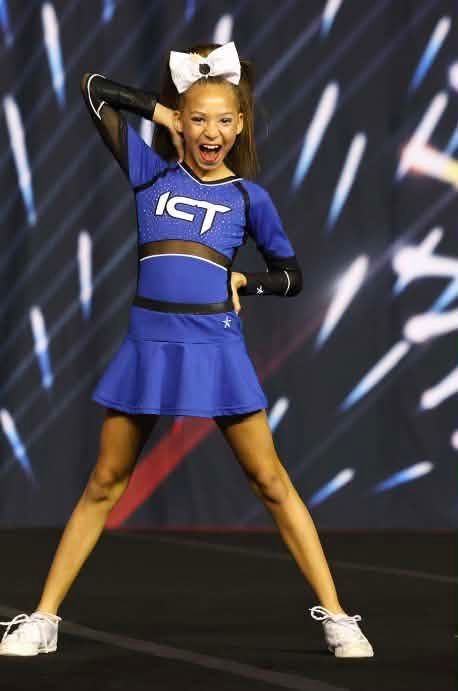 Cheerleader in blue ICT uniform posing on stage with arms raised and legs apart