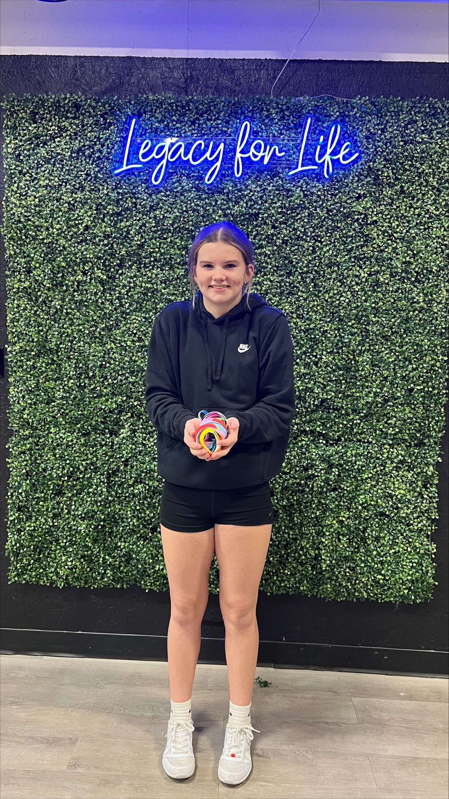 A young woman is standing in front of a neon sign that says legacy for life.