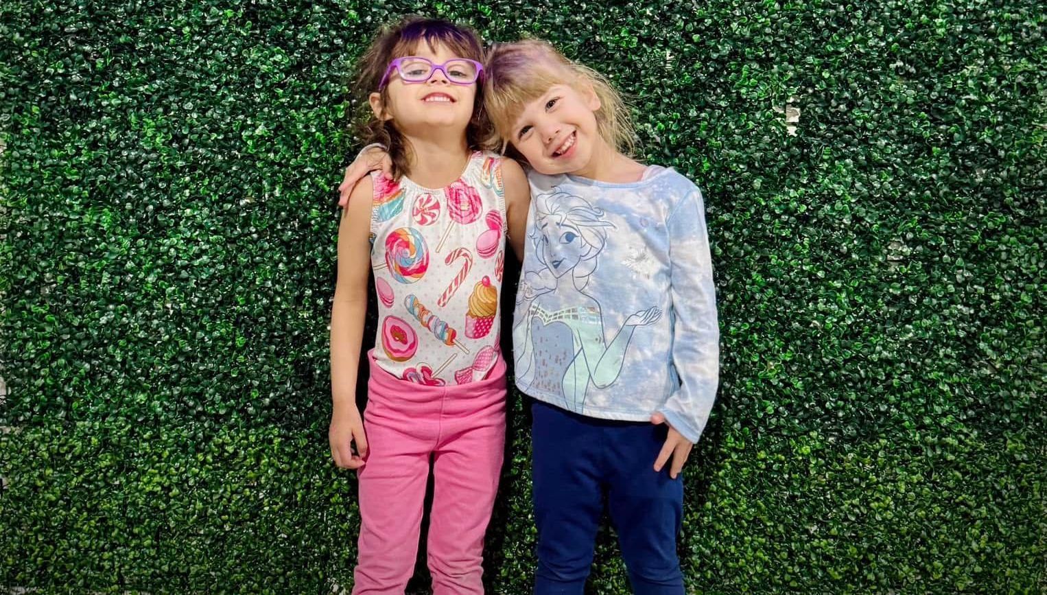 Two little girls are standing next to each other in front of a green wall.
