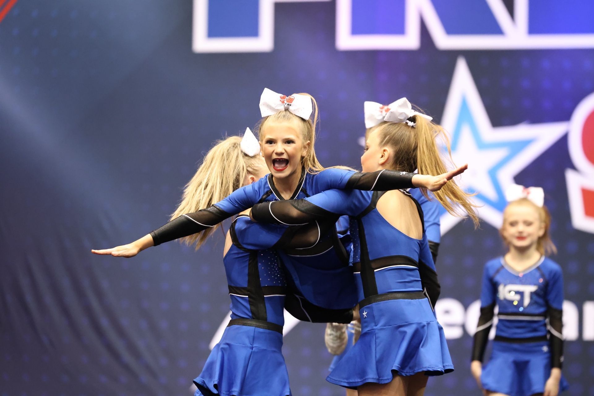 cheerleaders in blue uniforms performing a stunt with an excited expression on stage