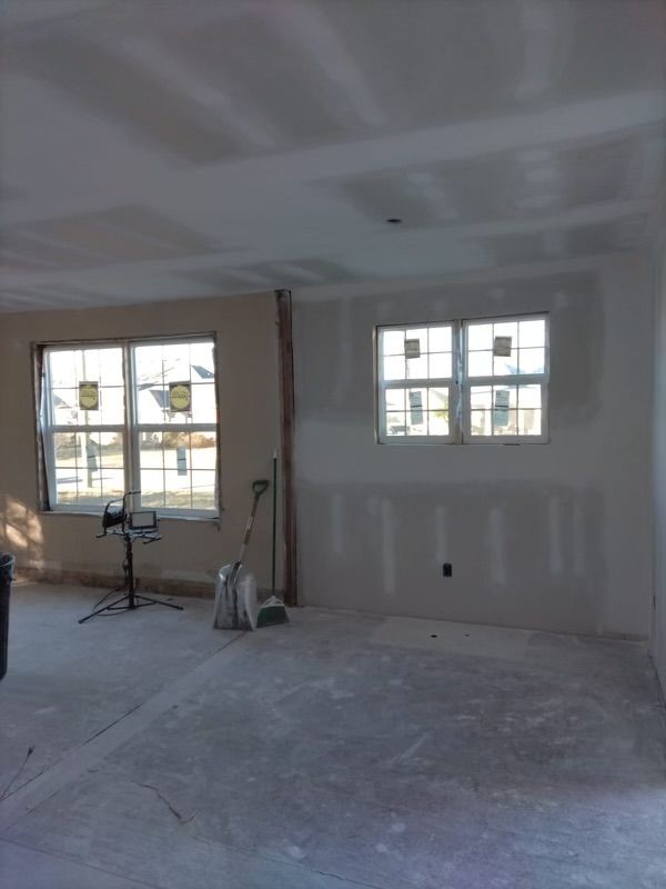 Interior of a room under construction with drywall, windows, and construction materials.