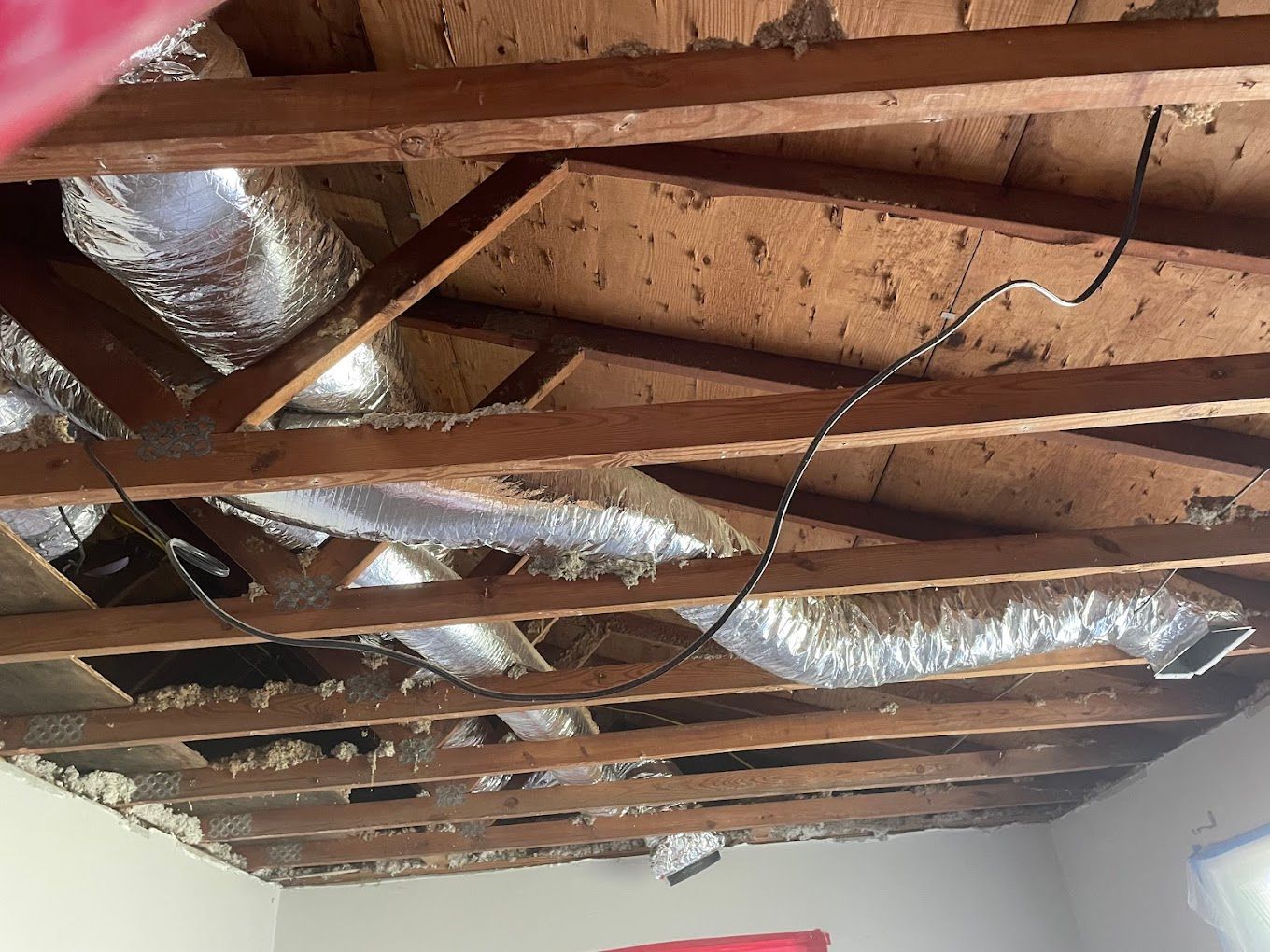 The open ceiling of a room with wooden beams and ducts