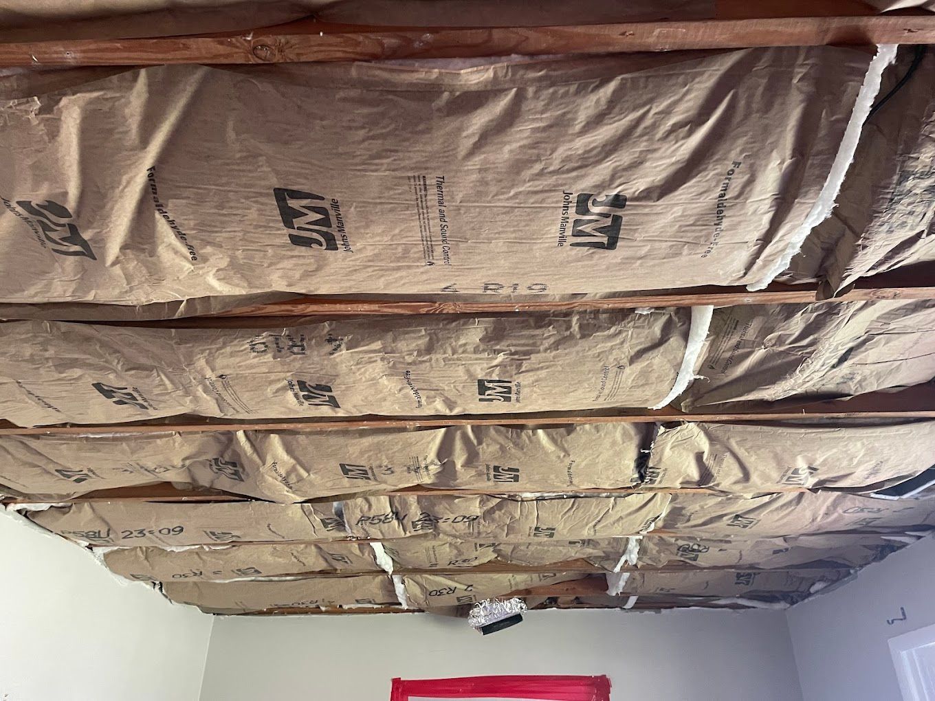 The open ceiling of a room with wooden beams and ducts