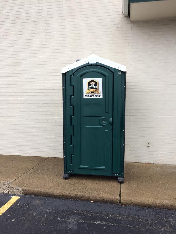 A green portable toilet is sitting on the sidewalk in front of a building.