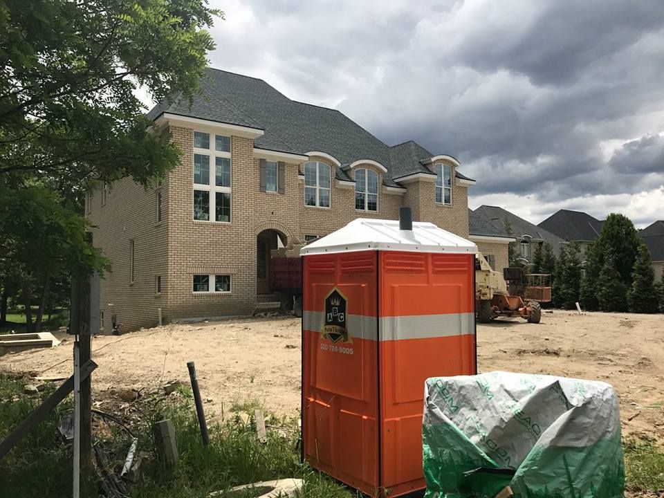 A large house under construction with a portable toilet in front of it.