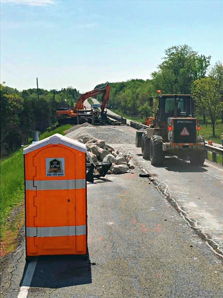 An orange portable toilet is sitting on the side of a road.