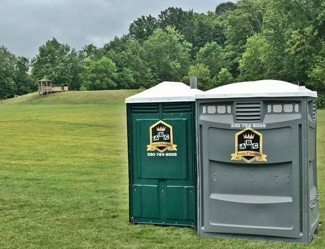 Two portable toilets are sitting next to each other in a grassy field.
