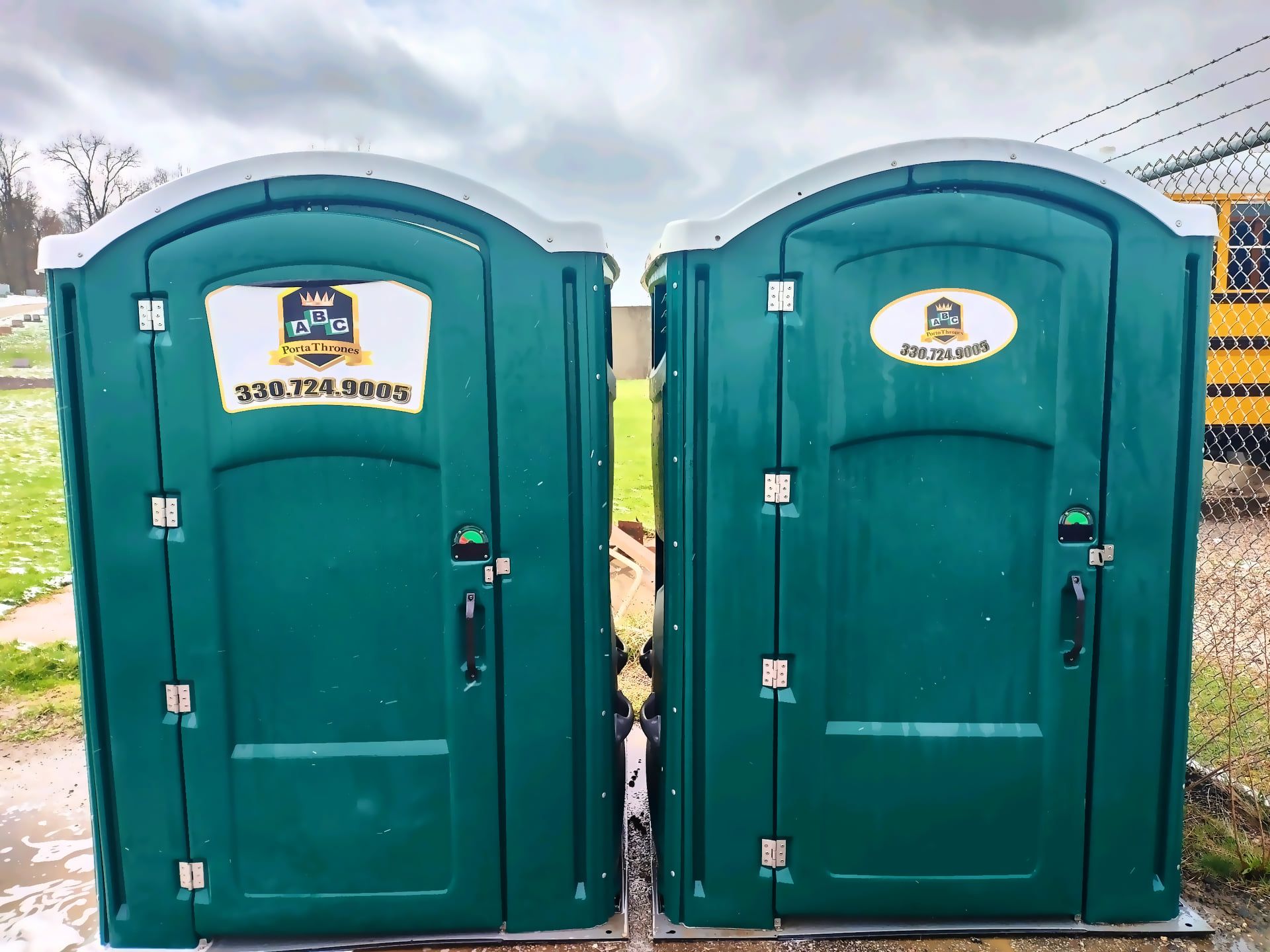 Two green portable toilets are sitting next to each other.