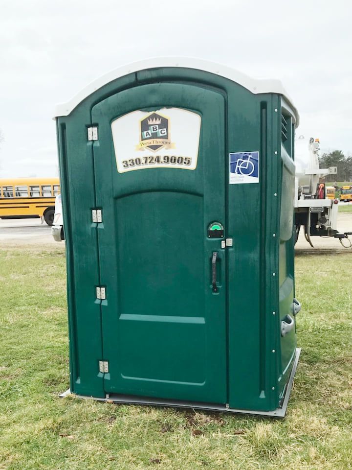 A green portable toilet is sitting on top of a lush green field.