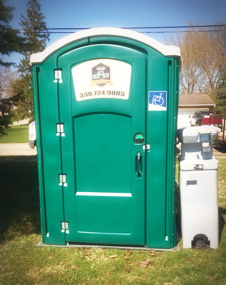 A green portable toilet with a handicap sign on the door
