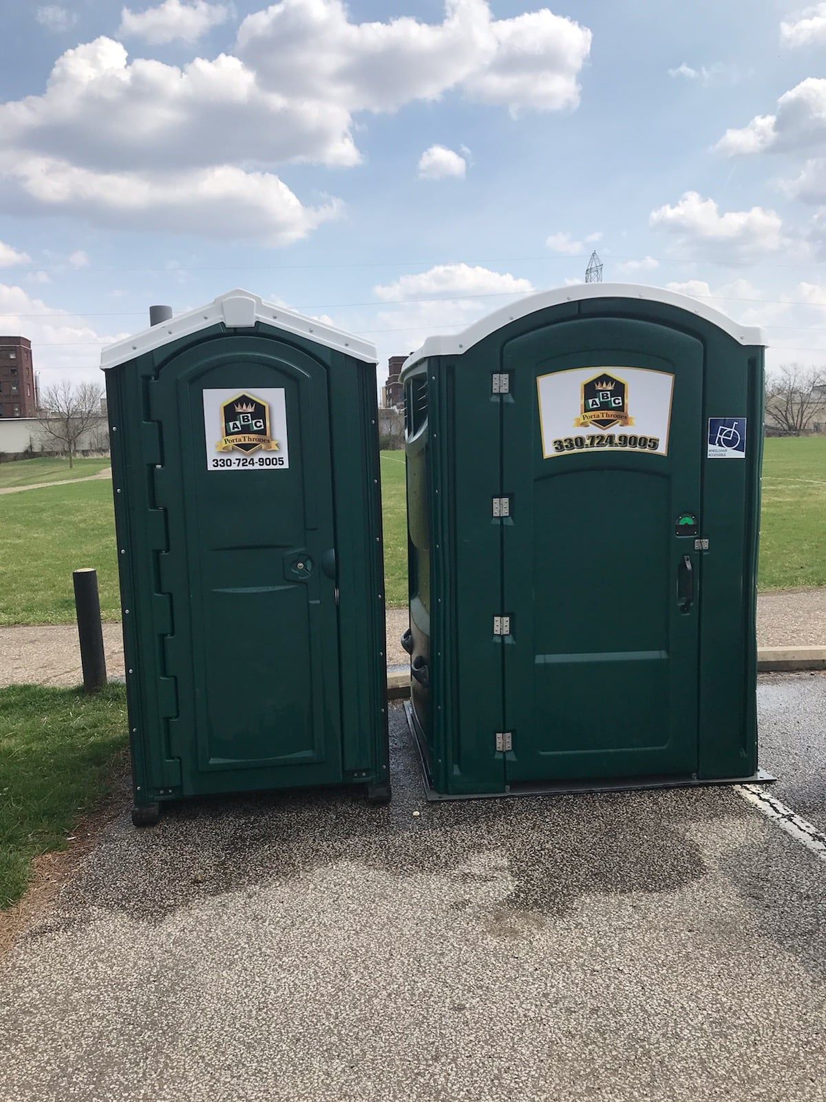 Two green portable toilets are sitting next to each other in a parking lot.