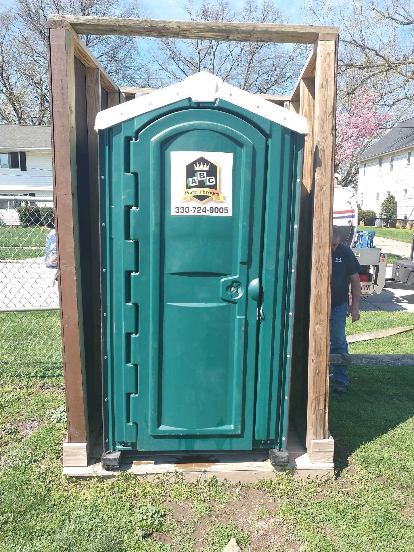 A green portable toilet is sitting in the grass