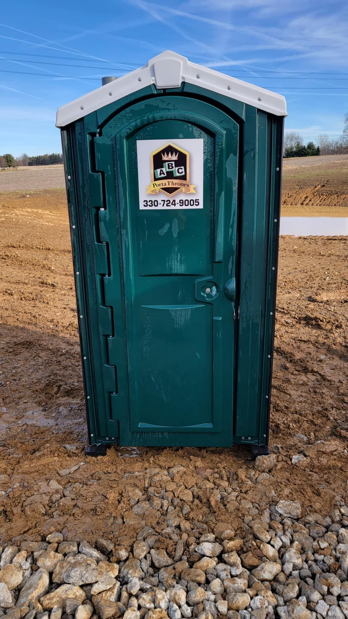 A green portable toilet is sitting on top of a pile of rocks.