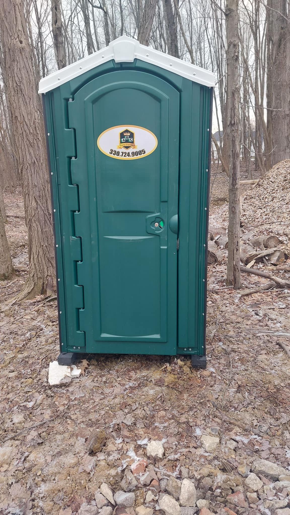 A green portable toilet is sitting in the middle of a forest.