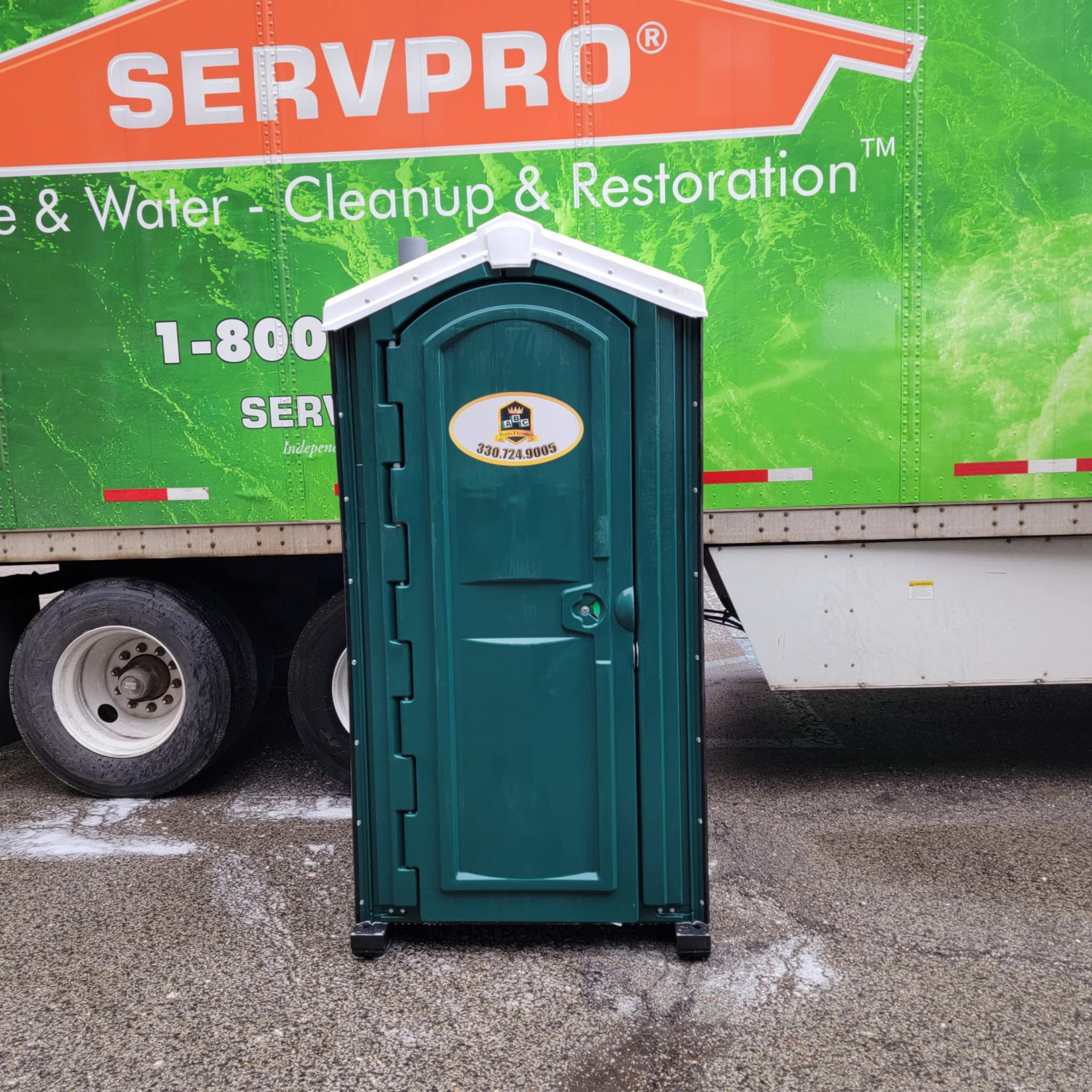 A green portable toilet is parked in front of a servpro truck