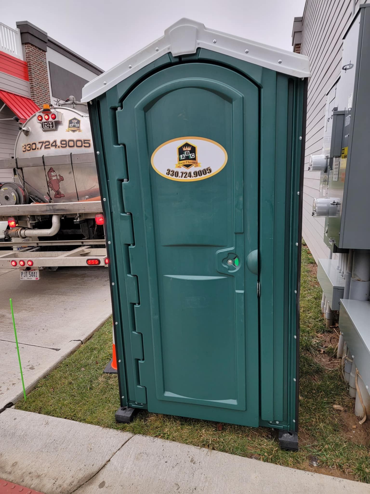 A green portable toilet is sitting on the sidewalk next to a truck.