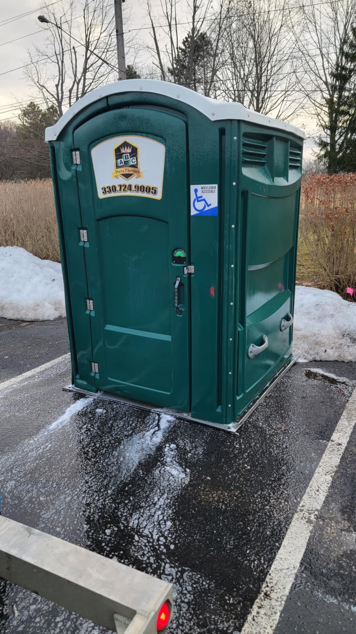 A green portable toilet is parked in a parking lot.