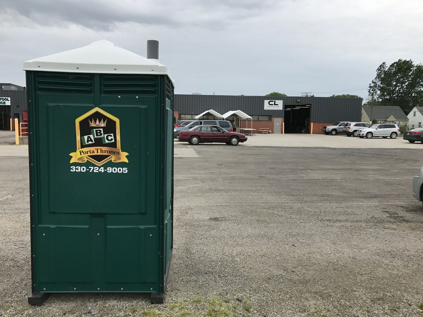 A green portable toilet is parked in a parking lot in front of a building.