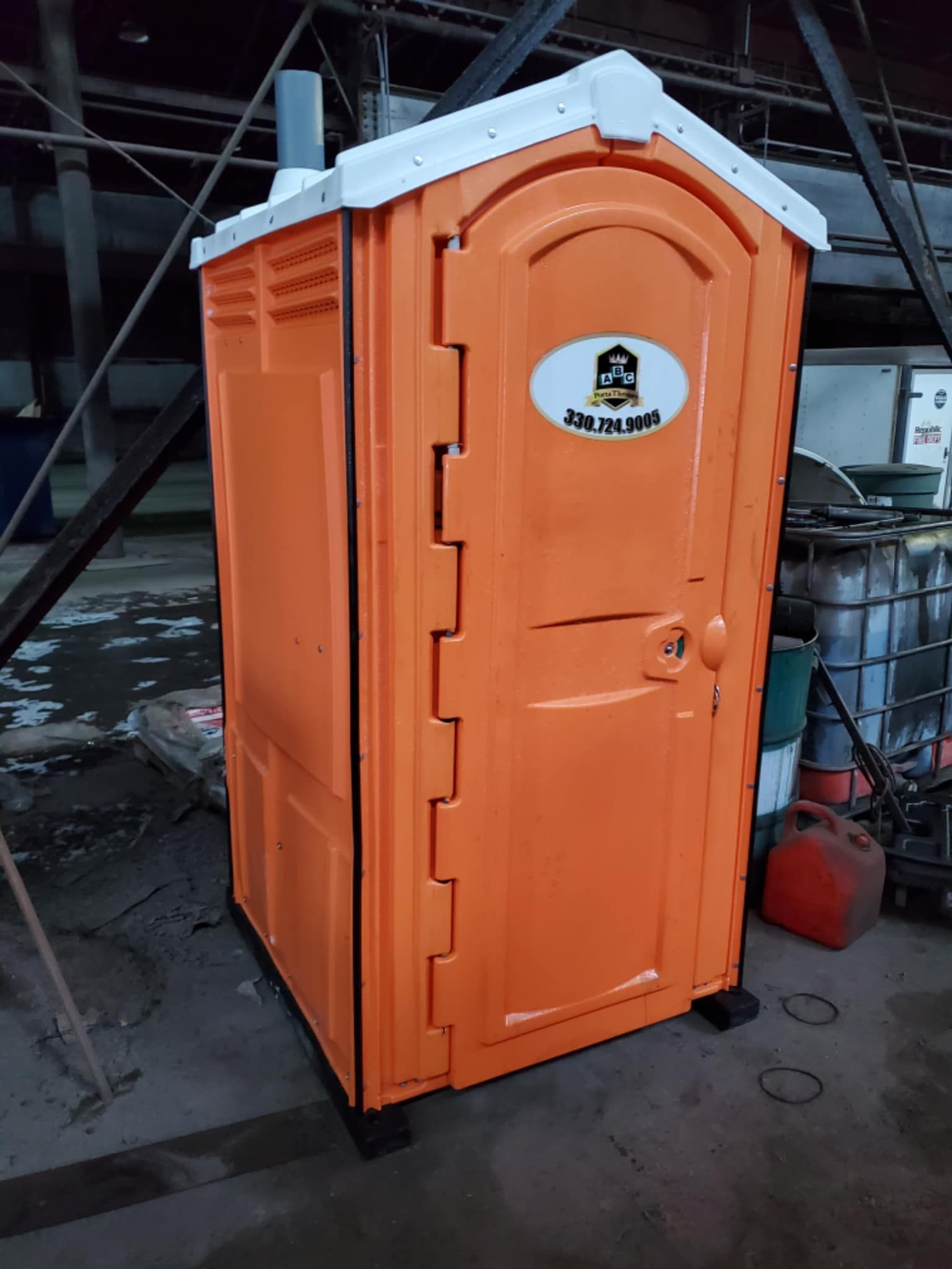 A small orange portable toilet is sitting in a warehouse.