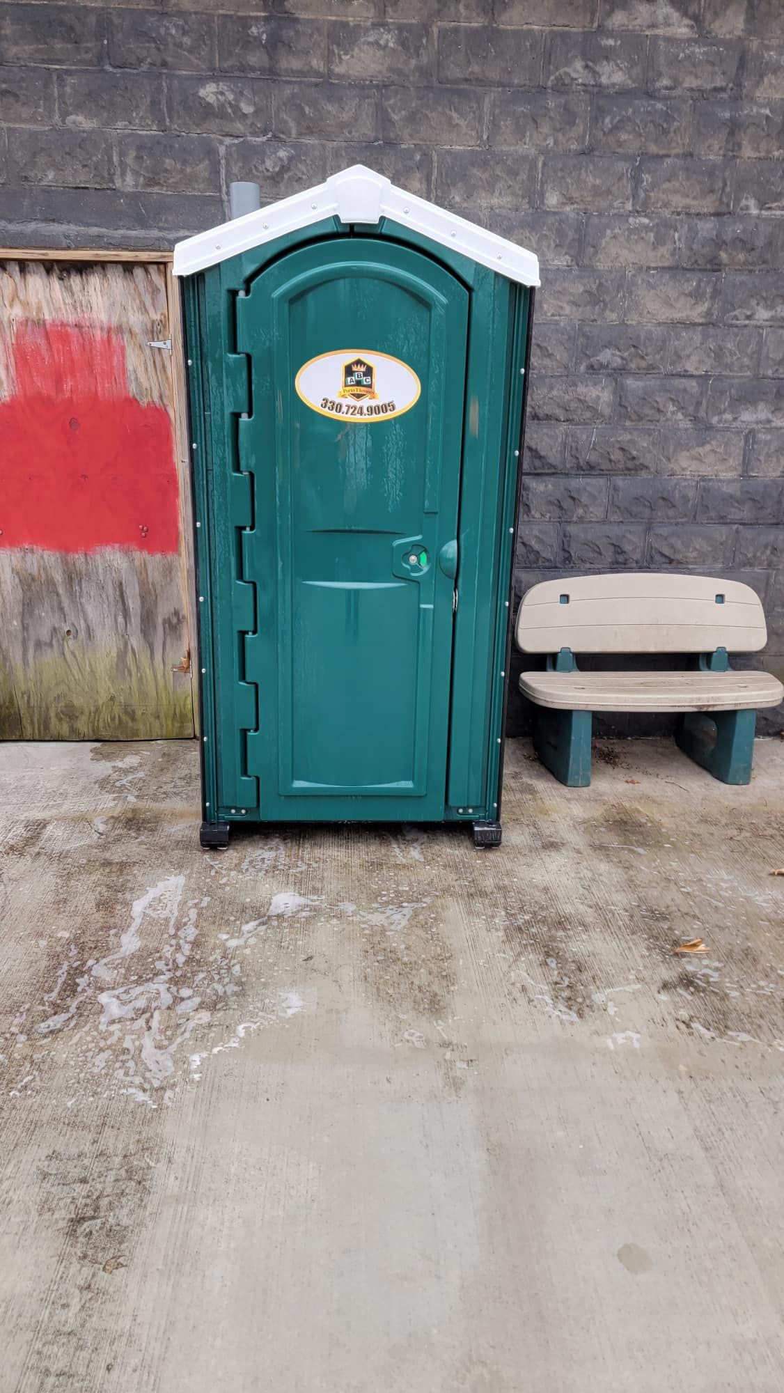 A green portable toilet is sitting next to a bench.