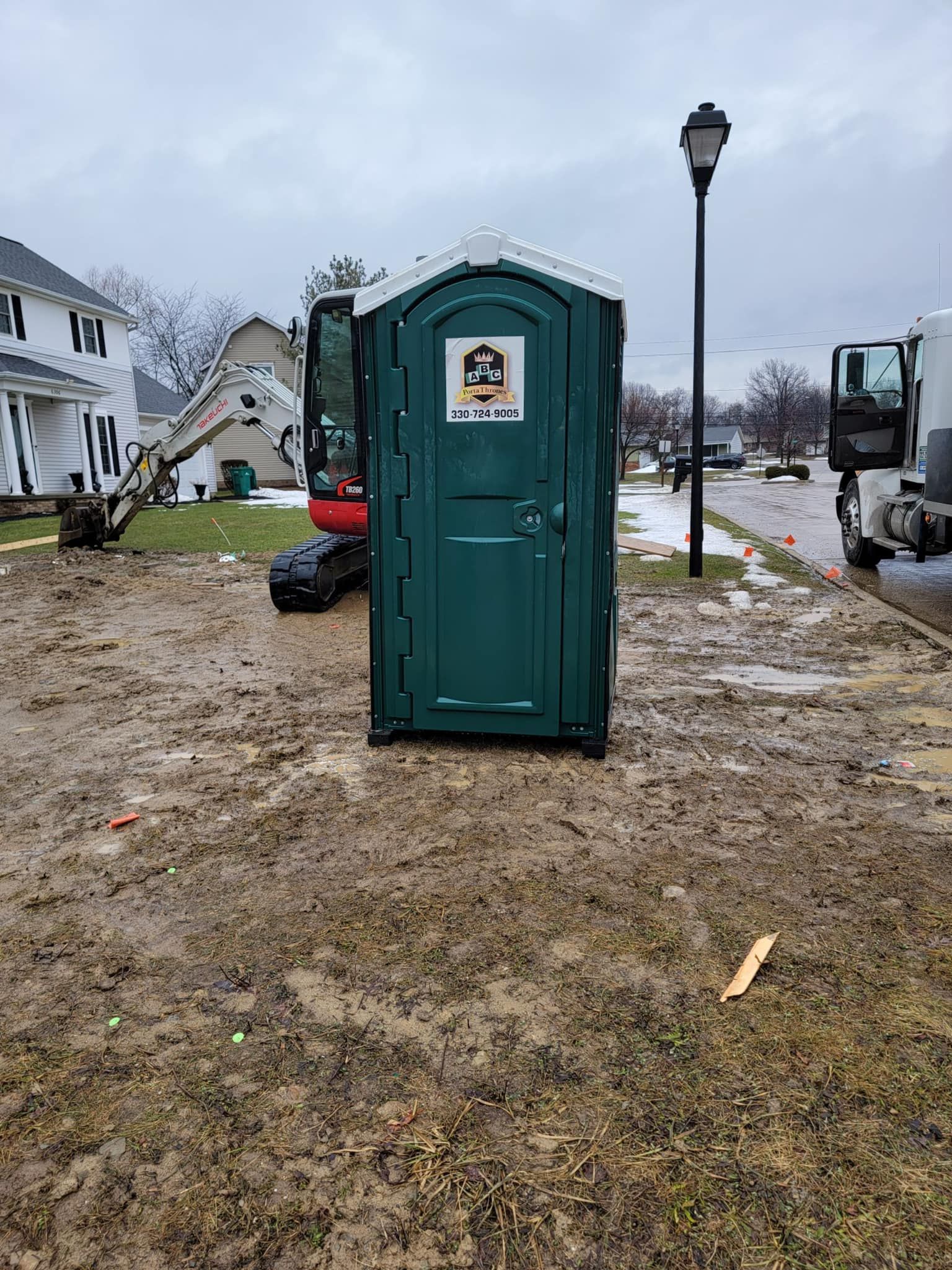 A green portable toilet is sitting in the middle of a dirt field.