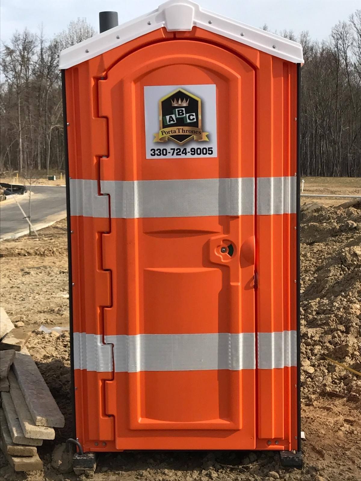 An orange portable toilet with a phone number on the door