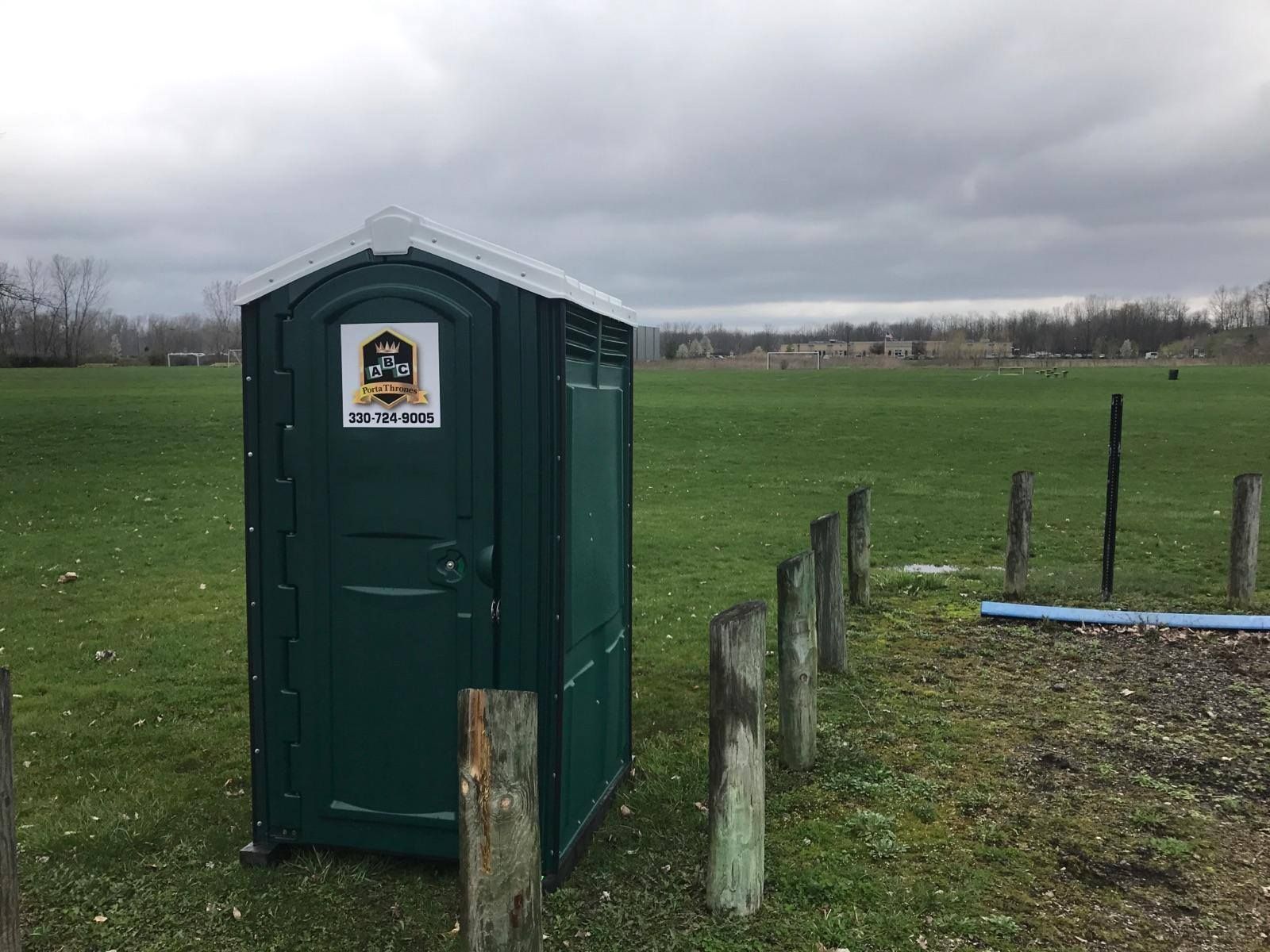 A green portable toilet is sitting in the middle of a grassy field.