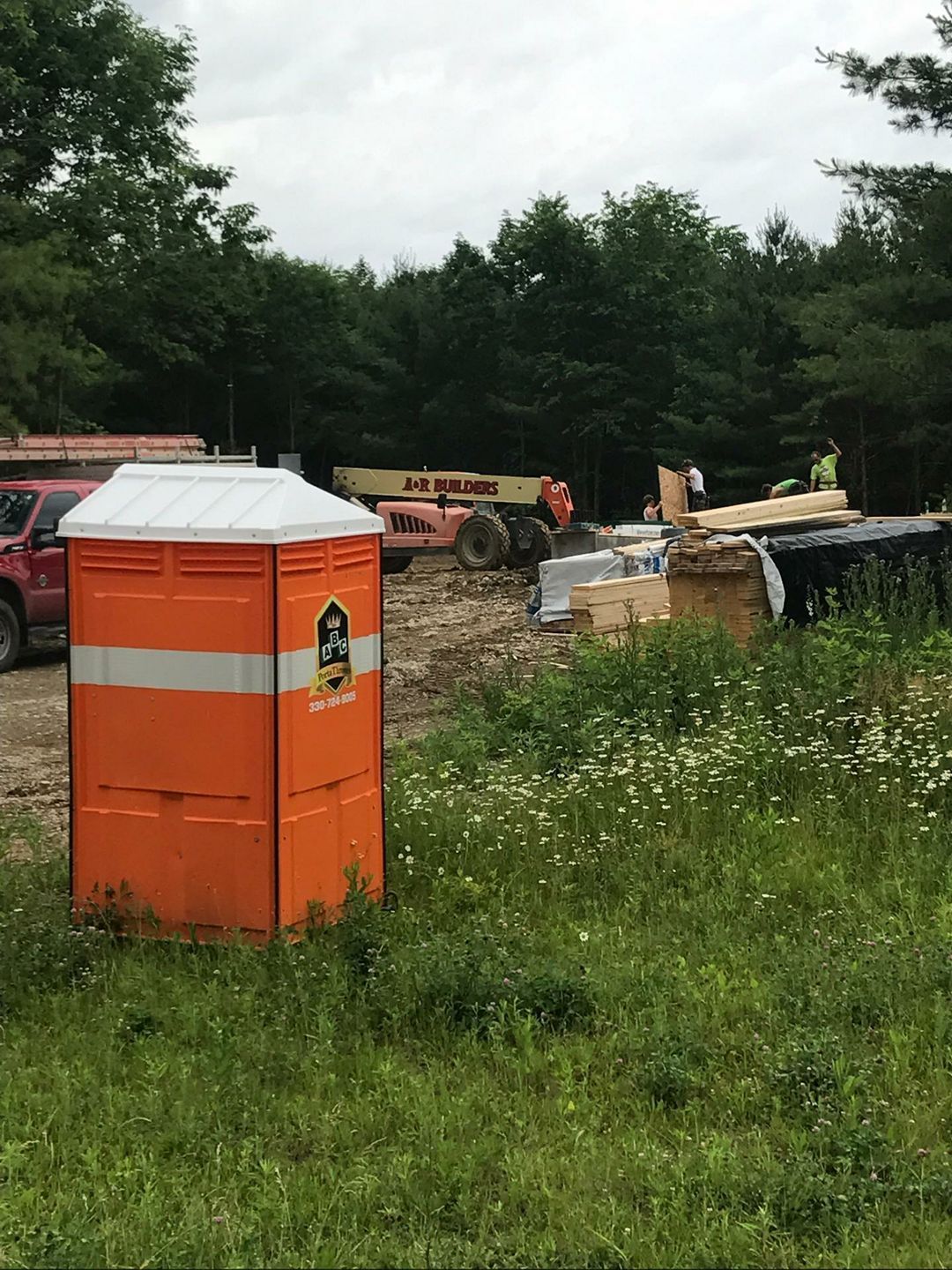 An orange portable toilet is sitting in the middle of a grassy field.