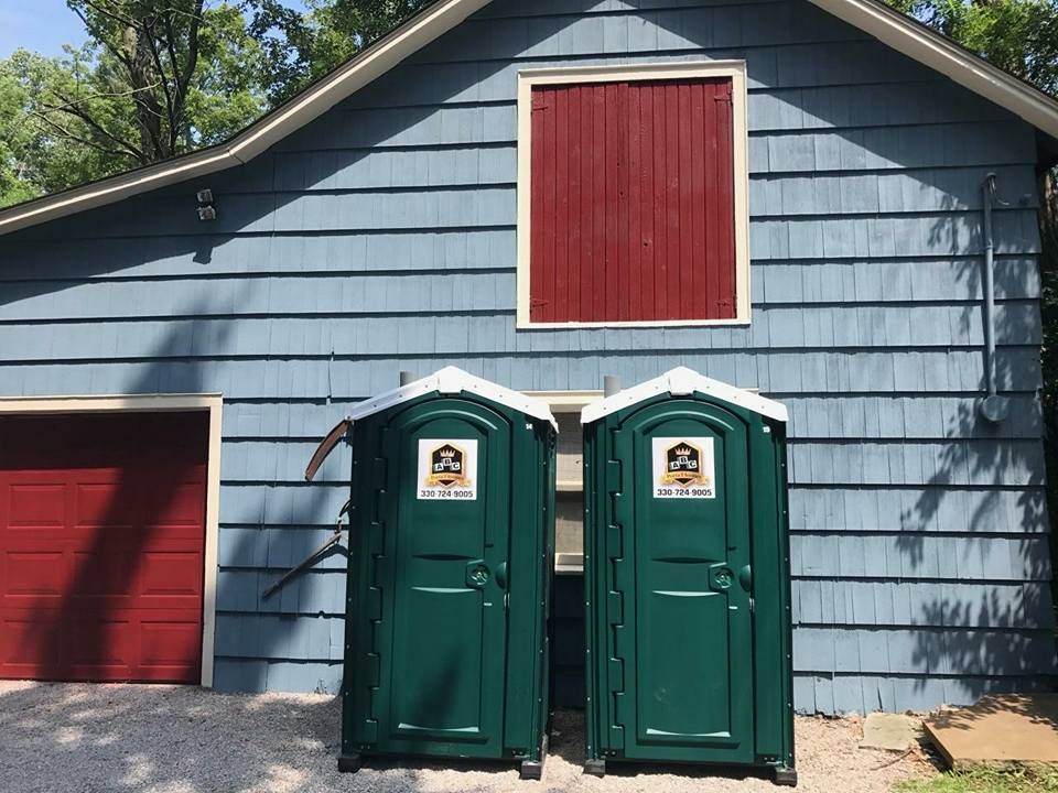 Two green portable toilets are in front of a blue house.