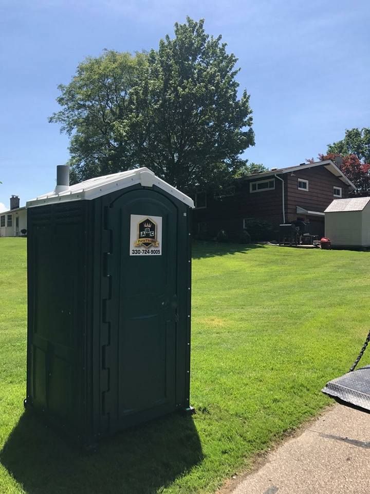 A green portable toilet is sitting in the middle of a grassy field.