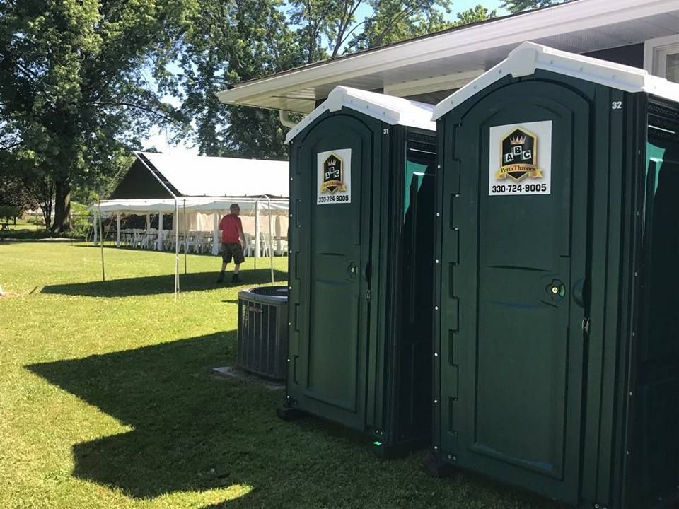 Two green portable toilets are sitting next to each other in a grassy field.