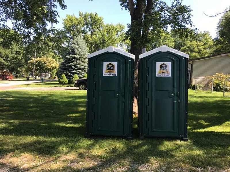 Two green portable toilets are sitting next to each other in a grassy field.