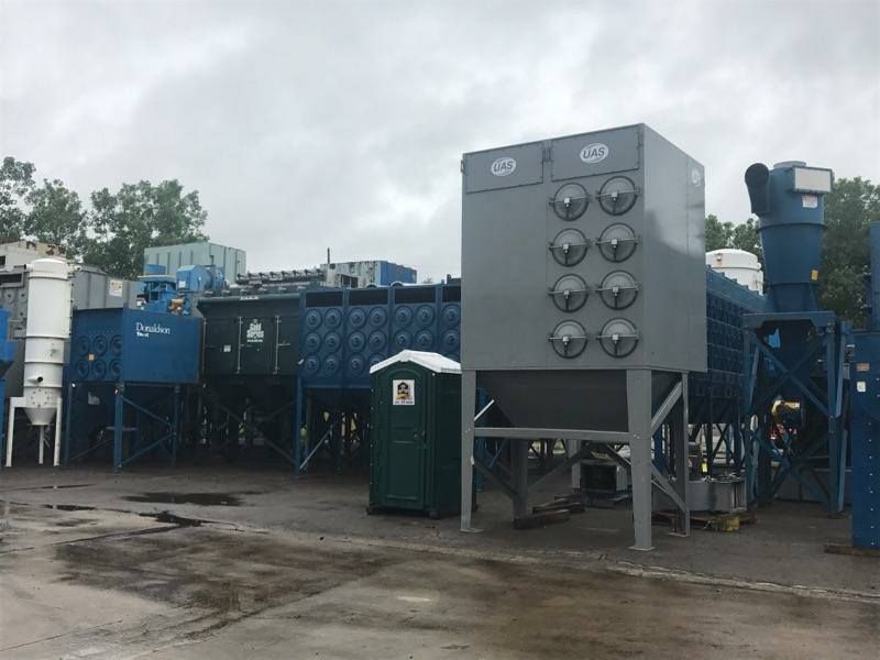 A green portable toilet is sitting next to a large machine in a parking lot.