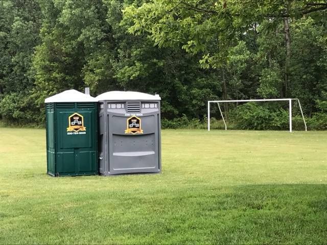 Two portable toilets are sitting on top of a lush green field next to a soccer goal.