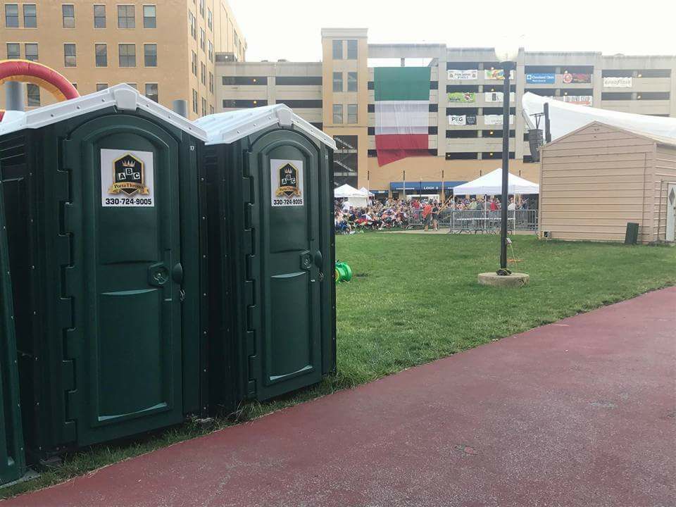 Two green portable toilets are sitting next to each other in a park.