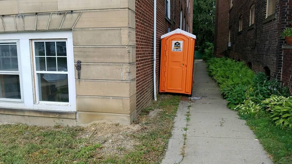 An orange portable toilet is sitting next to a brick building