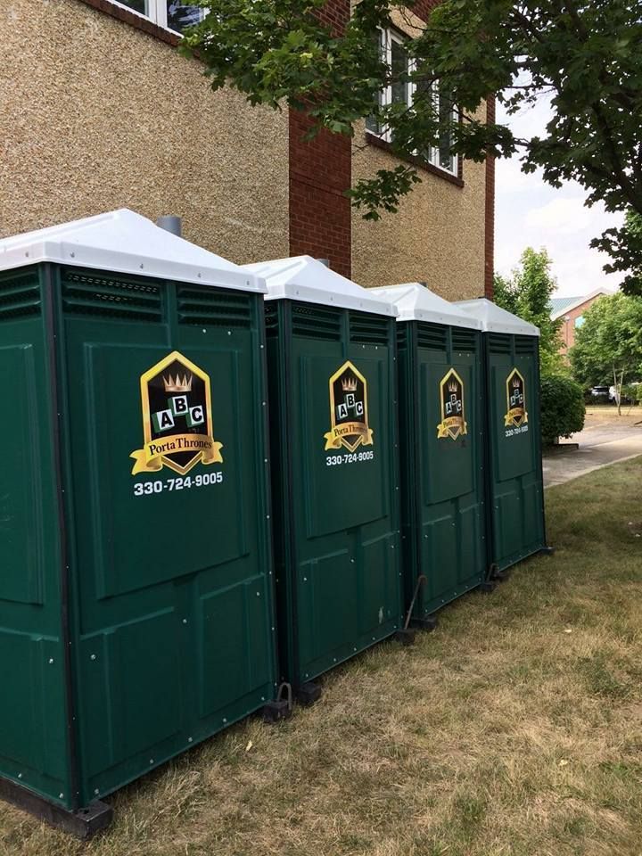 A row of green portable toilets are lined up in front of a building.