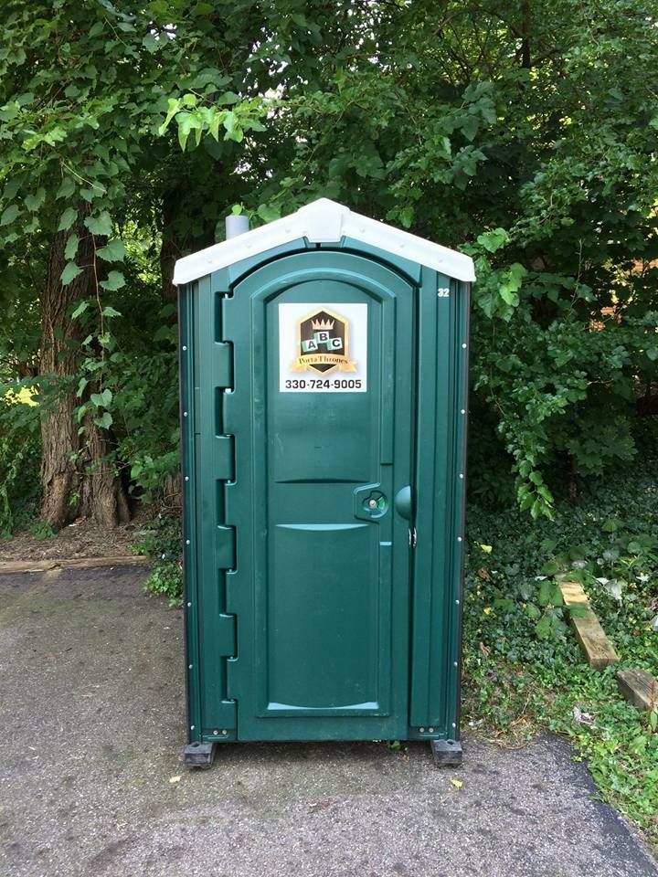 A green portable toilet is sitting on the side of a road.