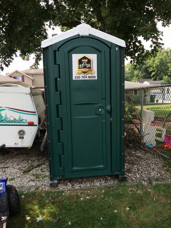 A green portable toilet is sitting in the grass next to a trailer.