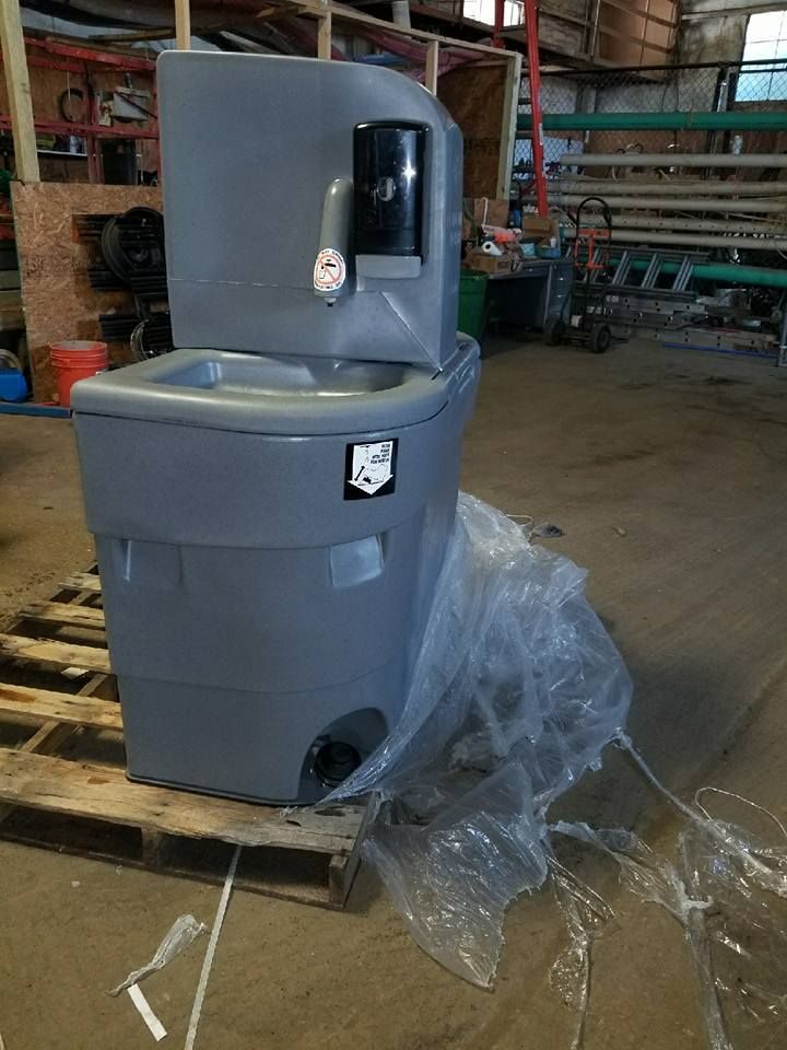 A portable sink is sitting on top of a wooden pallet in a warehouse.