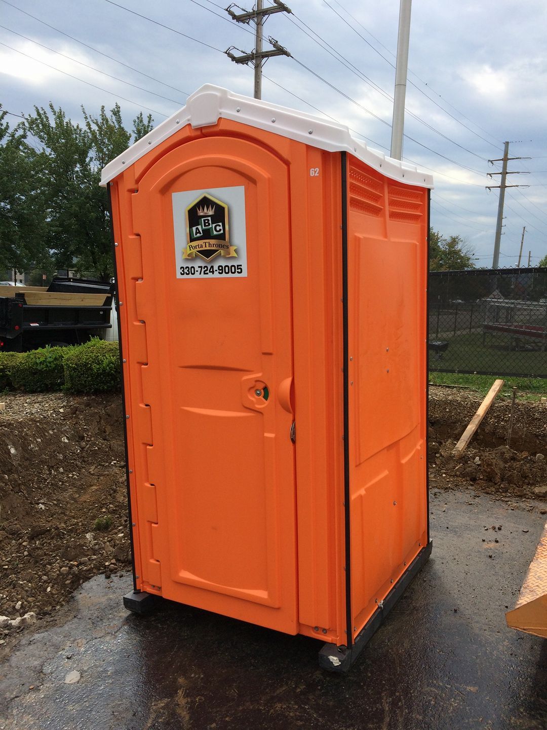 A small orange portable toilet is sitting on the side of the road.