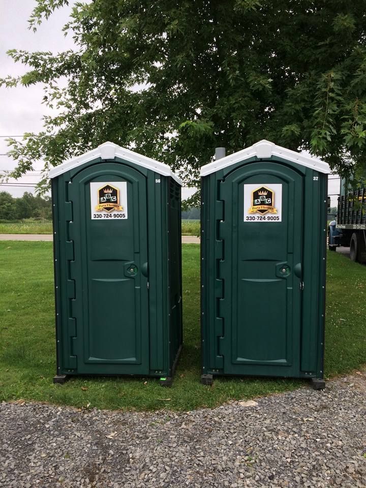 Two green portable toilets are sitting next to each other in a grassy field.