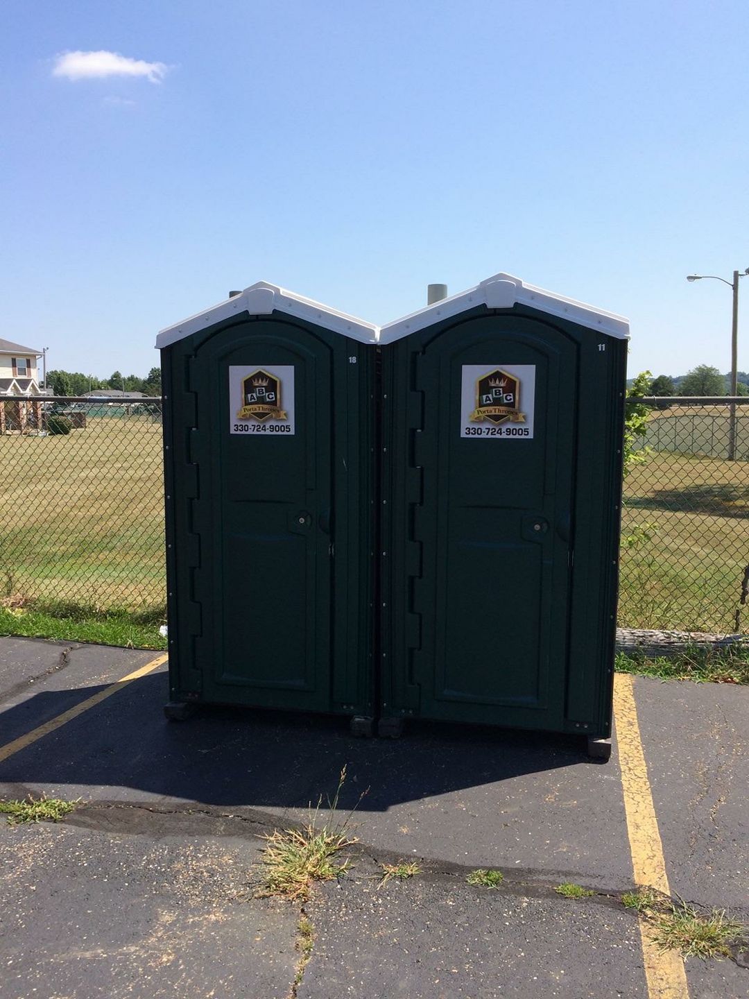 Two green portable toilets are sitting next to each other in a parking lot.