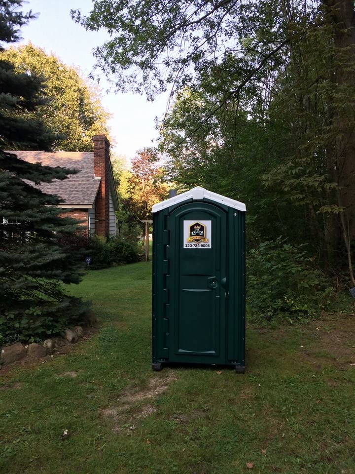 A green portable toilet is sitting in the grass in front of a house.