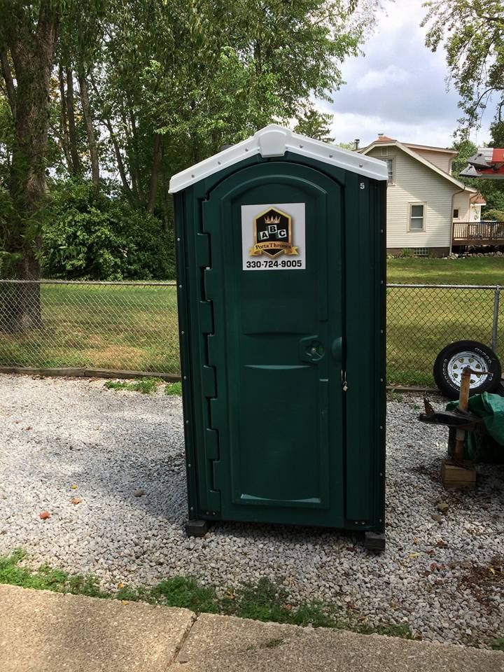 A green portable toilet is sitting on the side of the road next to a fence.