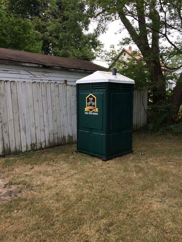 A green portable toilet is sitting in a backyard next to a white fence.