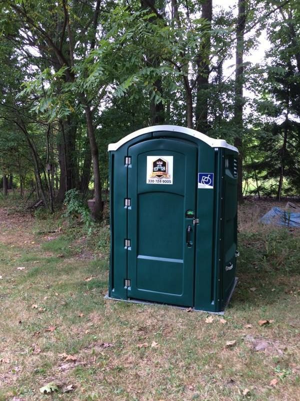 A green portable toilet is sitting in the middle of a grassy field.