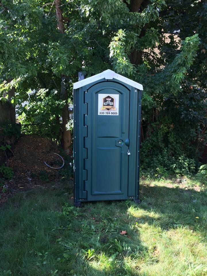 A green portable toilet is sitting in the grass.