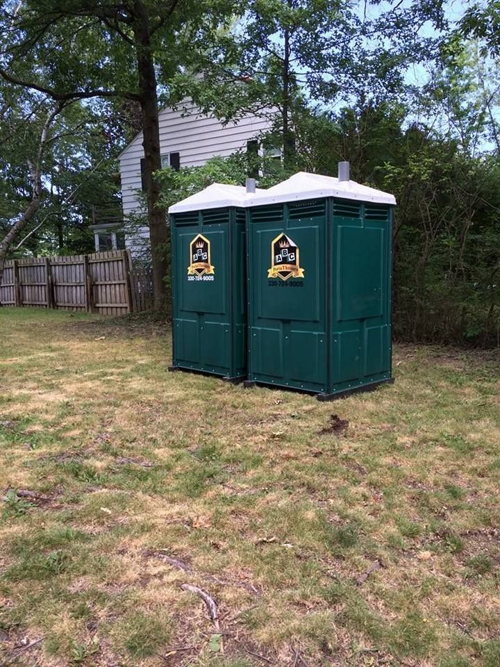 Two green portable toilets are sitting next to each other in a grassy field.